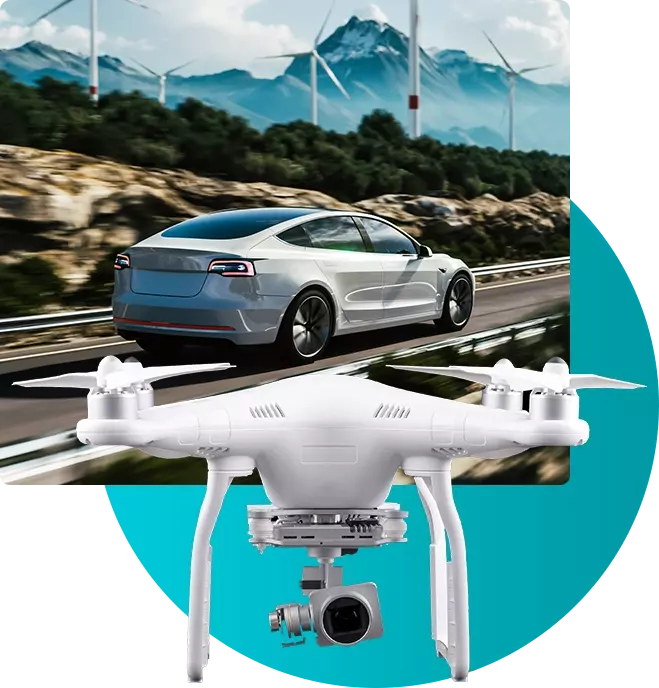 A drone flying besides a car driving along a road with power generating windmills
